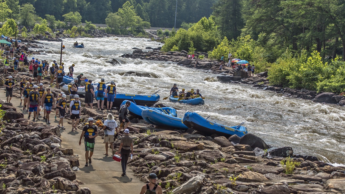 Large groups of people wearing helmets and life jackets walk along the Ocoee river to get to inflatable rafts